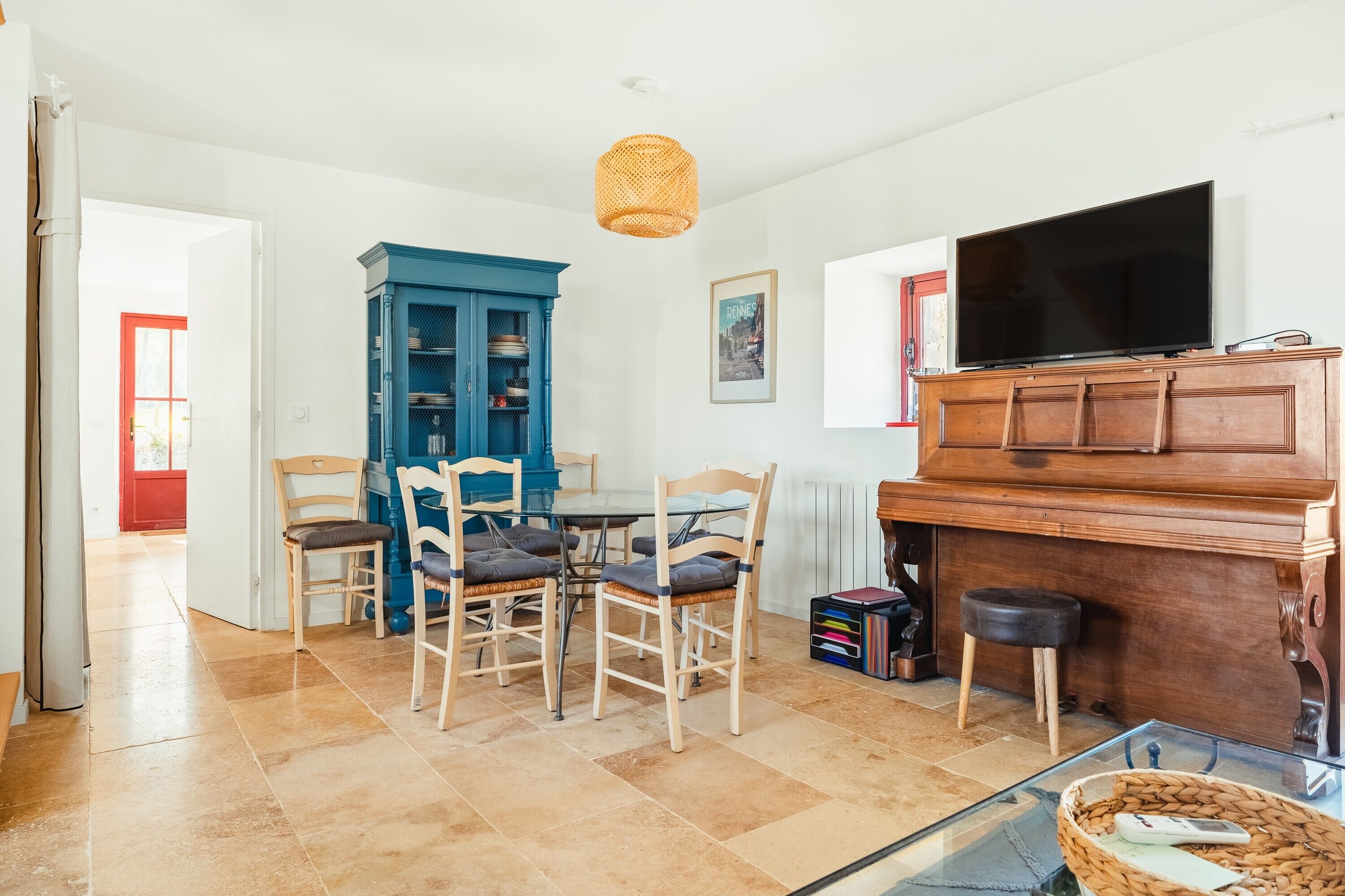 A living room with a dining table, chairs, a blue cabinet, a television, and a piano.