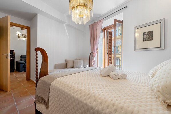 Un dormitorio con una cama, una araña, un cuadro enmarcado y vistas a través de una ventana.