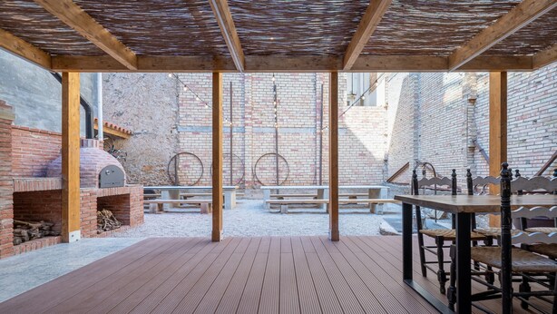 Une terrasse extérieure avec un four en briques, des tables et des bancs en bois.