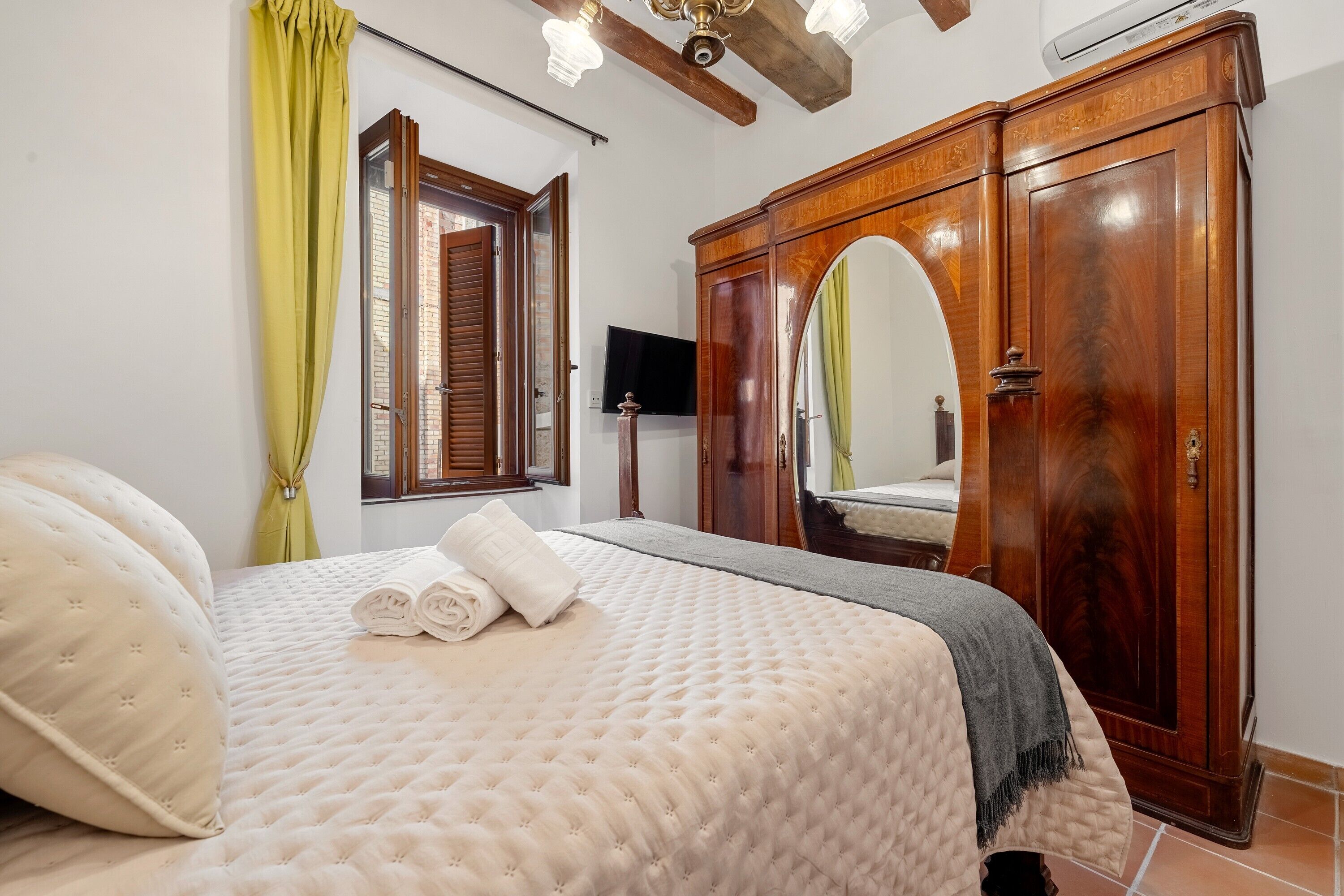 Un dormitorio con una cama, un armario de madera, un espejo y una ventana con cortinas.