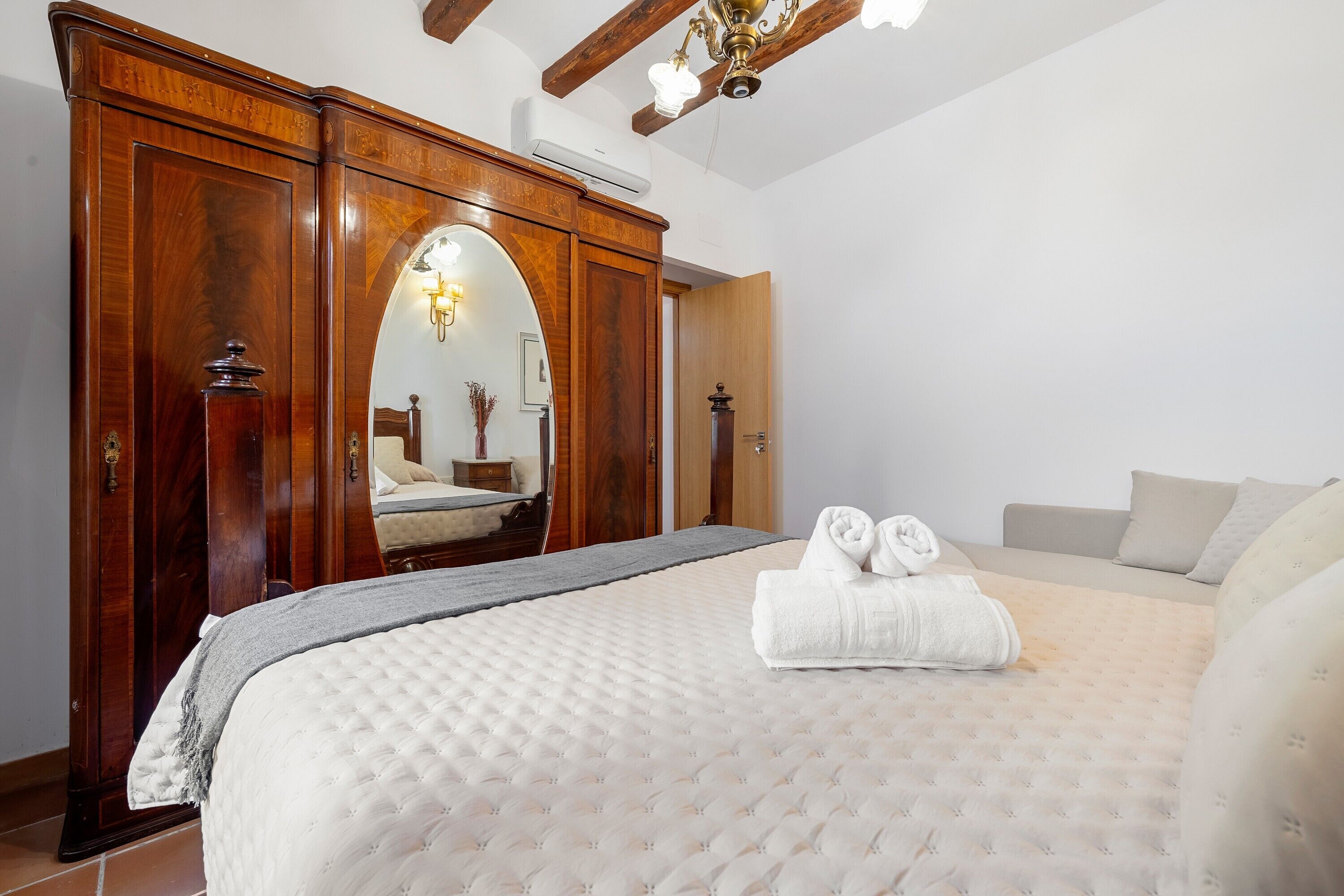 Un dormitorio con una cama grande, un armario de madera, un espejo y un ventilador de techo.