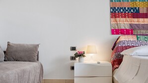 A bedroom with a bed, a nightstand with a lamp, and a colorful quilt on the wall. - Apartment 'Venere In Villa' with Shared Pool, Wi-Fi and Air Conditioning (Marina di Ragusa)