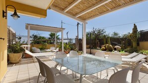 An outdoor patio with a glass table and white chairs, surrounded by potted plants and a pergola. - Apartment 'Venere In Villa' with Shared Pool, Wi-Fi and Air Conditioning (Marina di Ragusa)