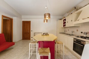 A modern kitchen with a central island, white cabinetry, and a red chair. - Apartment 'Athena In Villa' with Shared Pool, Wi-Fi and Air Conditioning (Marina di Ragusa)