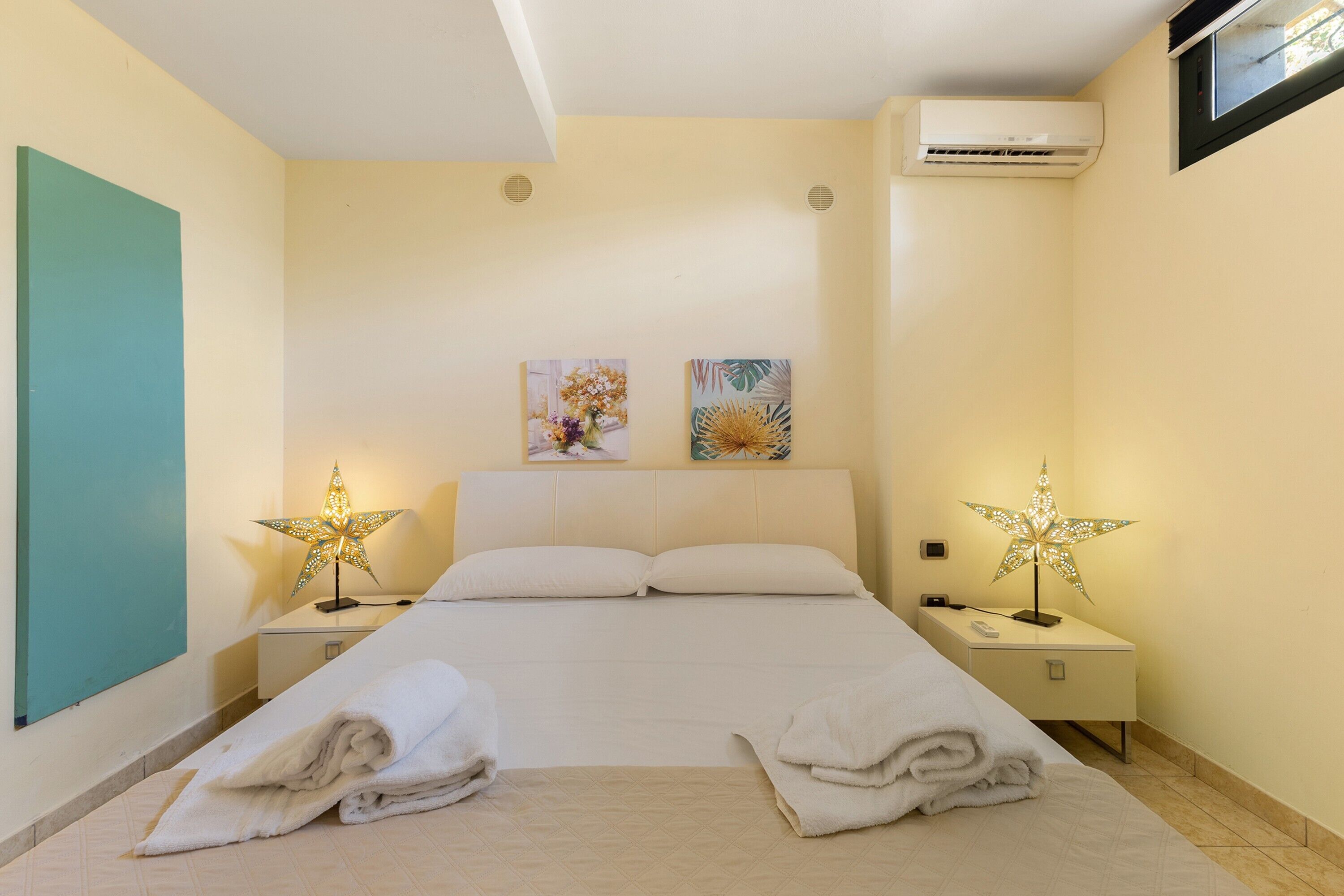 Ein Hotelzimmer mit einem Bett, zwei Bildern, einer Klimaanlage und einem Nachttisch mit einer Lampe.