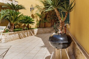 A patio area with a barbecue grill, palm trees, and a stone wall. - Apartment 'Athena In Villa' with Shared Pool, Wi-Fi and Air Conditioning (Marina di Ragusa)