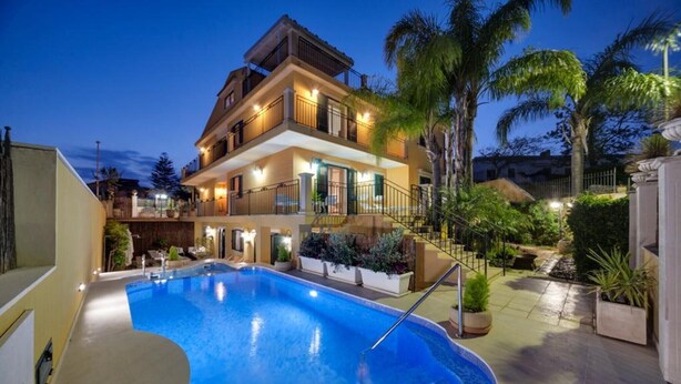 A multi-story building with a swimming pool, outdoor lighting, and tropical landscaping. - Apartment 'Athena In Villa' with Shared Pool, Wi-Fi and Air Conditioning (Marina di Ragusa)