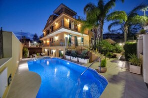 Un immeuble à plusieurs étages doté d’une piscine, d’un éclairage extérieur et d’un aménagement paysager de style tropical.