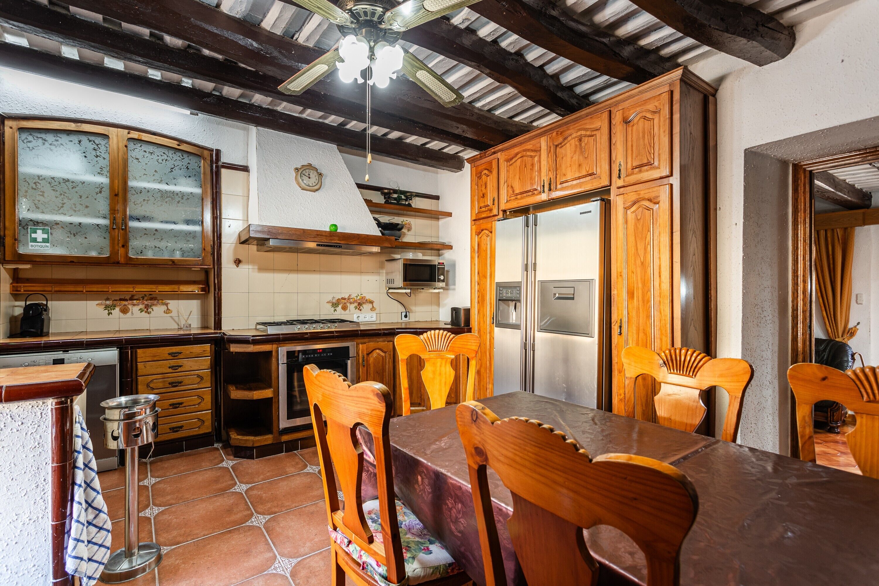 Une cuisine avec des meubles de rangement en bois, une table à manger avec des chaises, un ventilateur de plafond et un four à micro-ondes.