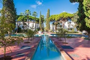 A swimming pool with a reflection, surrounded by trees and buildings.