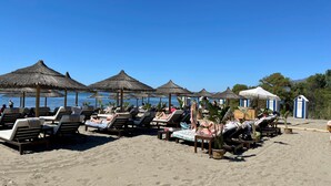 Una playa con tumbonas y sombrillas de paja.