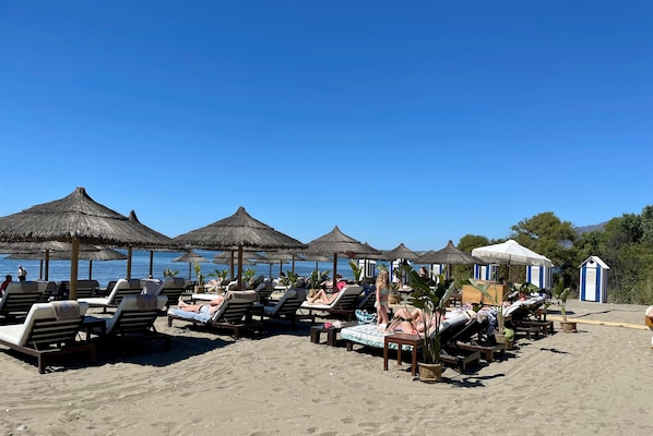 A beach with sun loungers and thatched umbrellas.