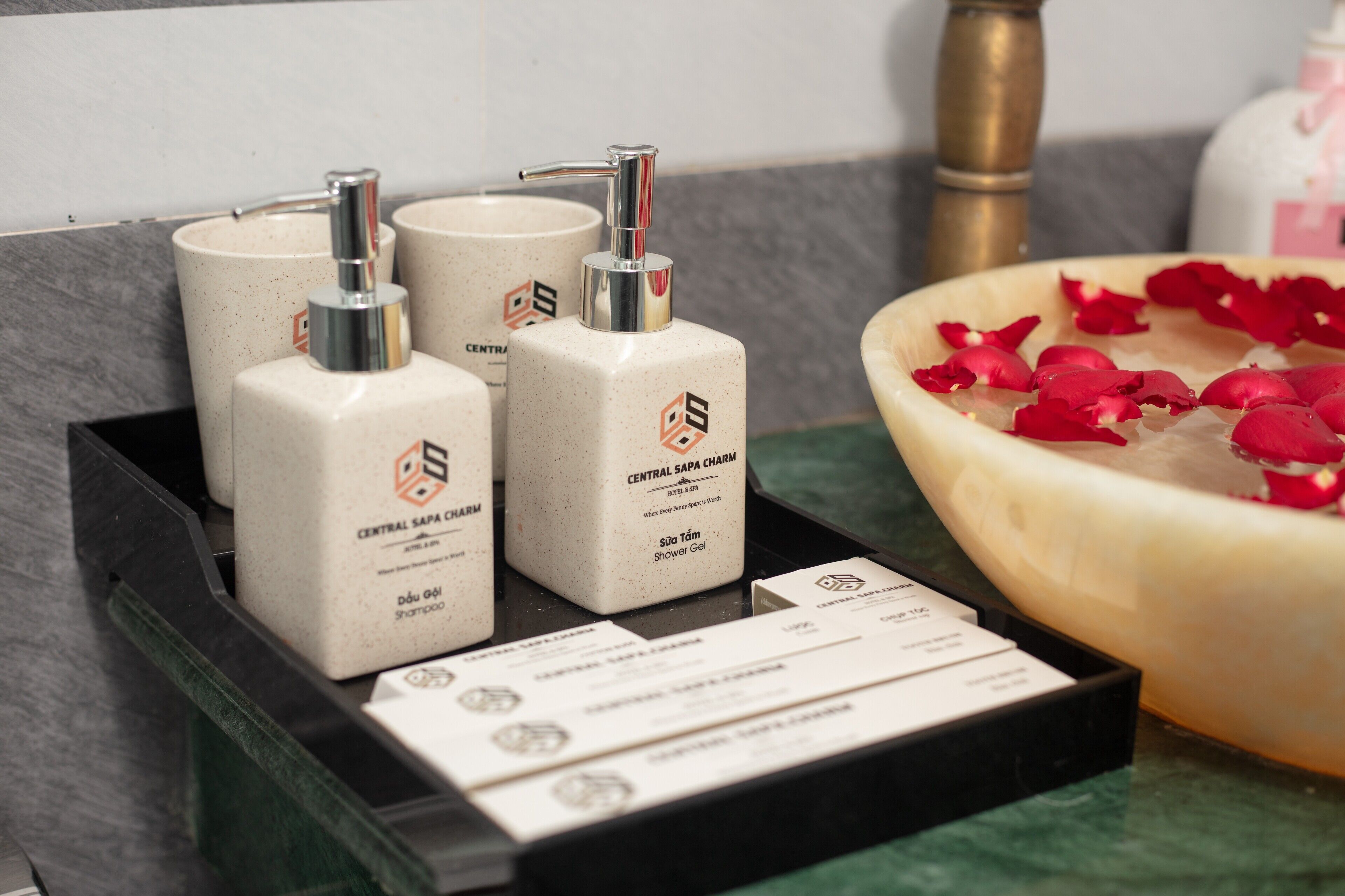 A display of Central Sapa Charm shower gel bottles and a bowl of rose petals.
