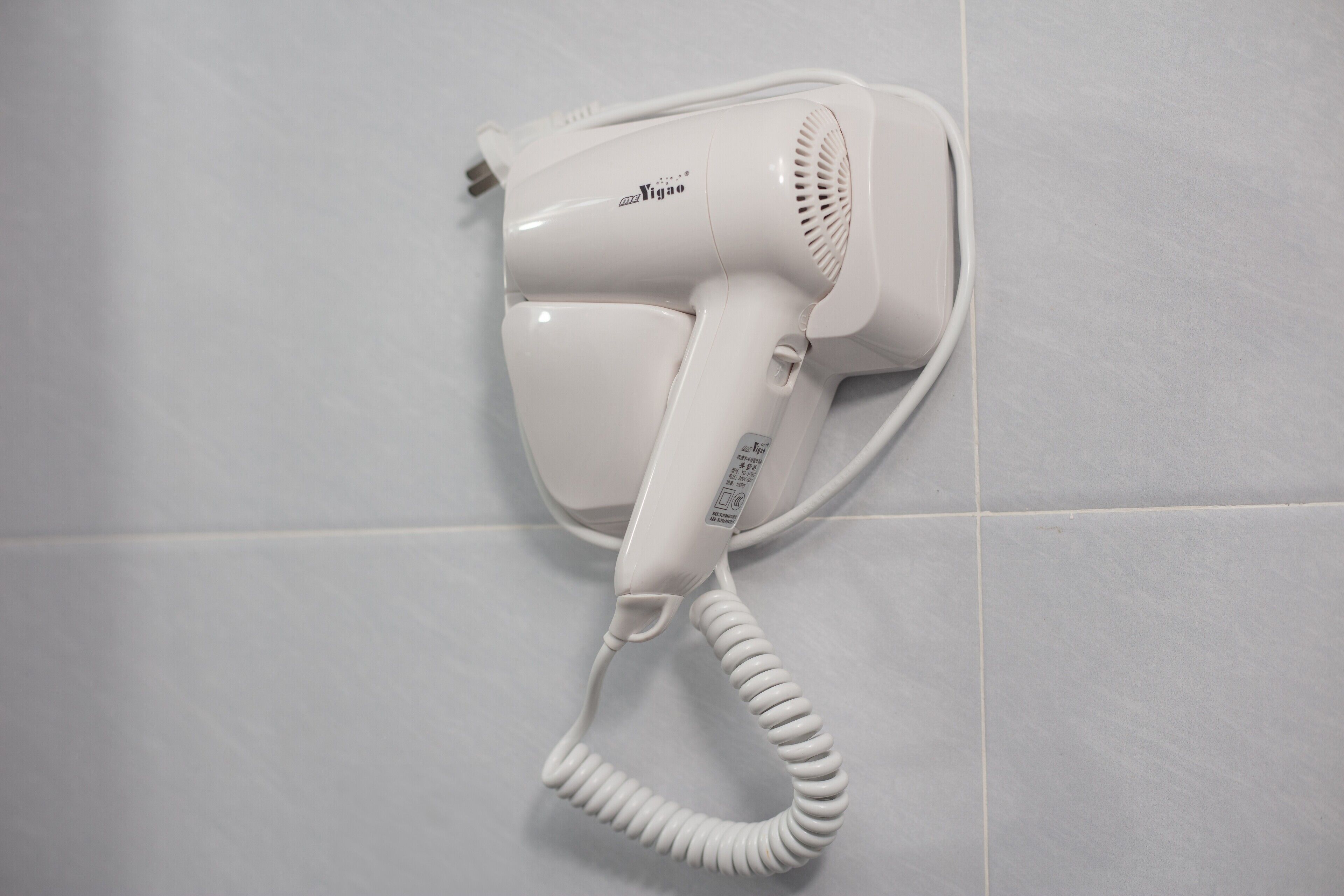 A white hair dryer mounted on a tiled wall.