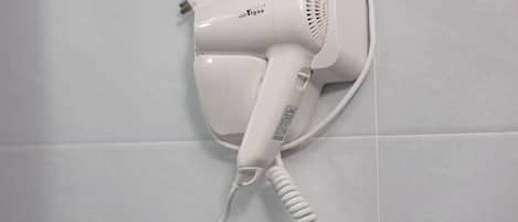 A white hair dryer mounted on a tiled wall.