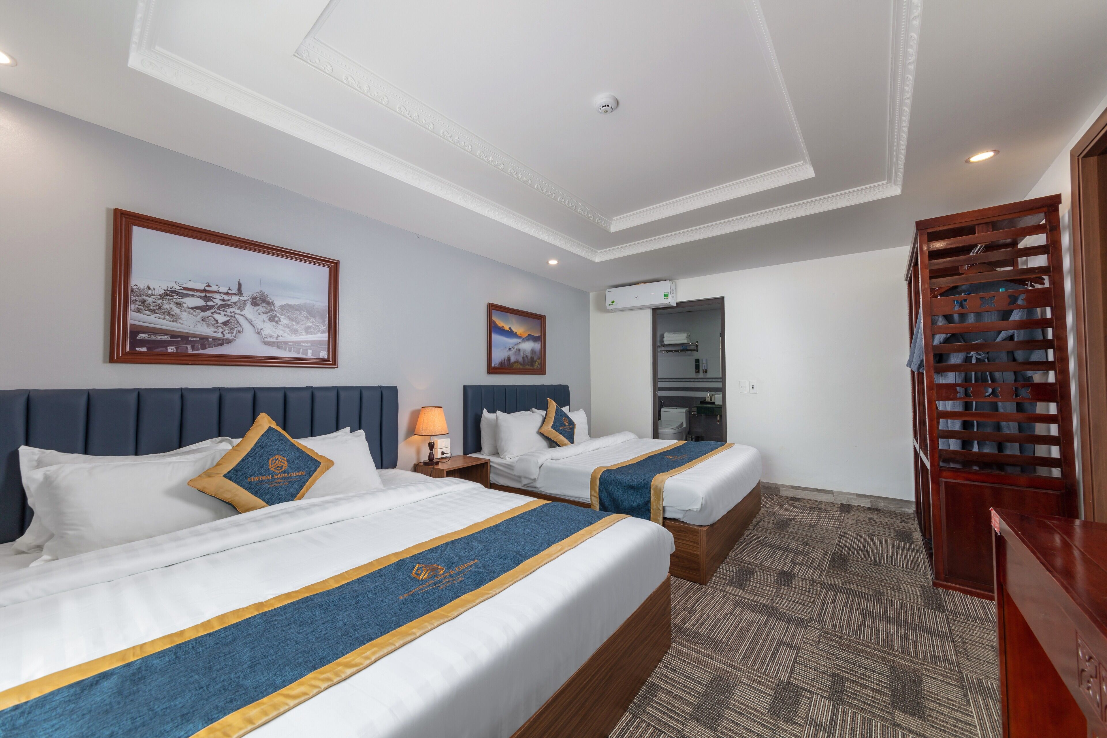 Habitación de hotel con dos camas, un techo con luz empotrada, un cuadro enmarcado en la pared y un escritorio de madera.