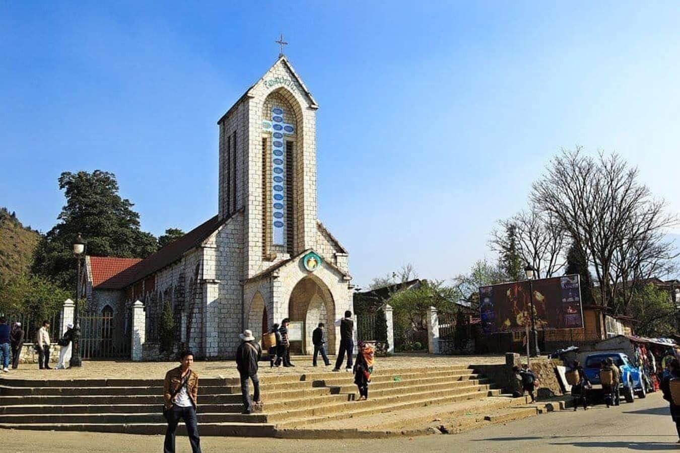 A church with a tall tower and arched entrance, surrounded by steps and a few people.