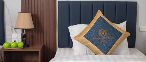 A neatly made bed with a blue headboard, a bedside table with a lamp, and three green apples on the table.
