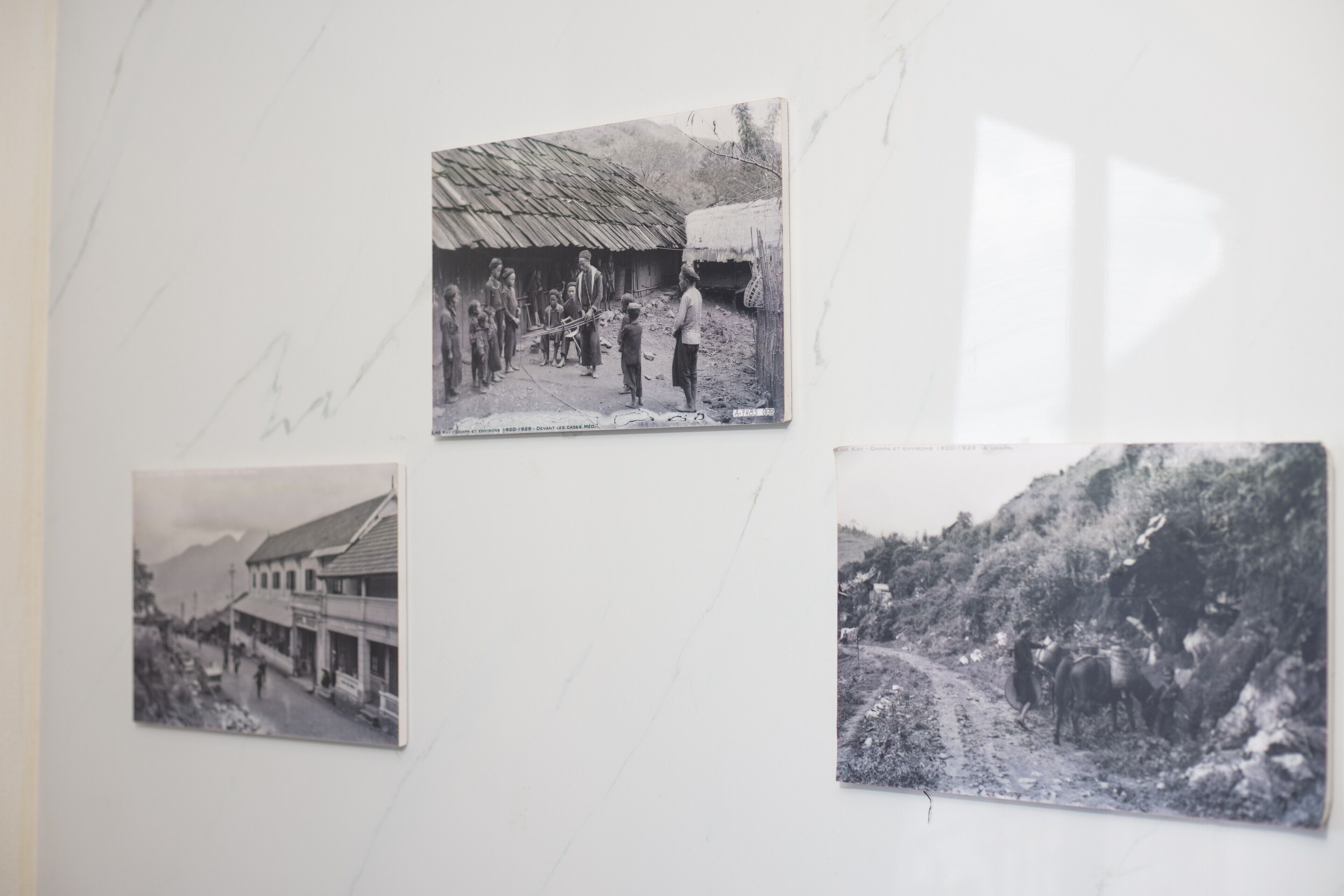 Una pared con tres fotografías blanco y negro que muestran un paisaje rural, un edificio con techo de paja y un paisaje montañoso.