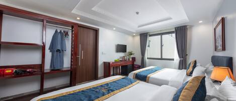 Una habitación de hotel con dos camas, un escritorio con televisor, un armario y una ventana con cortinas.