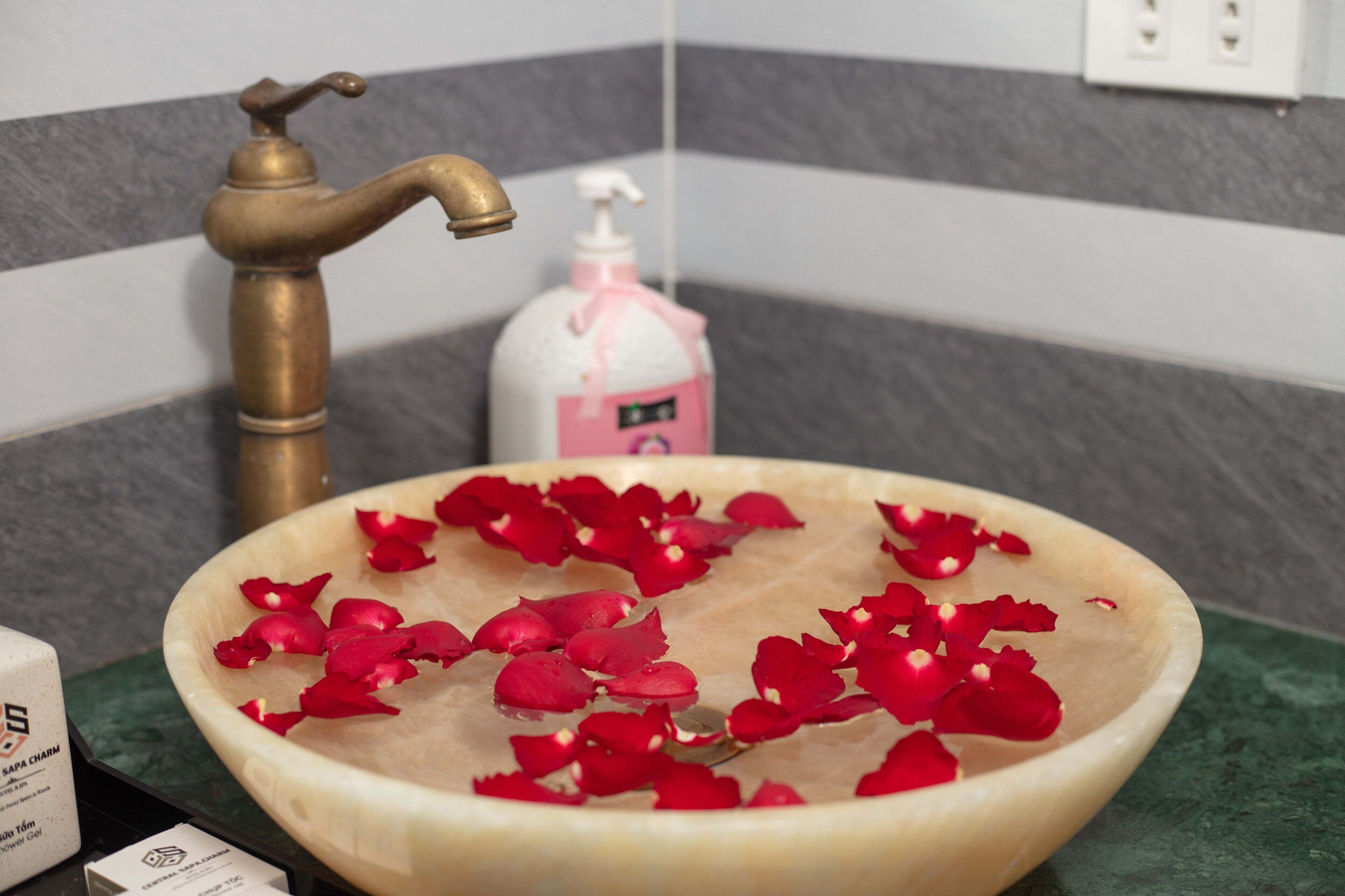 A bathroom sink with rose petals, a brass faucet, and a soap dispenser.