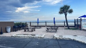 Une terrasse au bord de la plage, avec des tables de pique-nique et des parasols, offrant une vue sur l’océan.