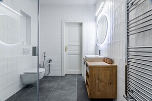 Une salle de bain moderne avec des murs recouverts de carreaux blancs, un meuble-lavabo en bois, des toilettes et une cabine de douche en verre.