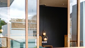 Ein modernes Interieur mit einer Glastür, die zu einem Außenbereich führt, einer hölzernen Bank und einem kleinen Tisch mit einer Lampe.