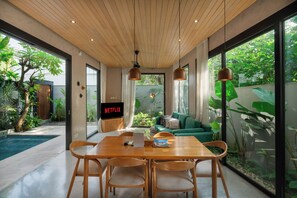 Un salon moderne avec un plafond en bois, un canapé vert, une table à manger en bois avec des chaises, et un écran de télévision affichant le logo « NETFLIX ».