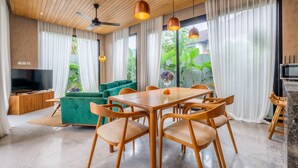 Ein modernes Wohnzimmer mit Holzboden, einem grünen Sofa, einem Holzesstisch mit Stühlen und einem Fernseher.