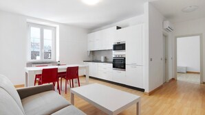Et moderne køkken med hvide skabe, et spiseområde med en rød stol, og en sofa.