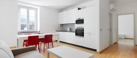 A modern kitchen with white cabinets, a dining area with a red chair, and a sofa.
