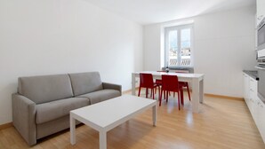 En moderne lejlighed med en grå sofa, et hvidt spisebord med røde stole og et køkken.