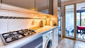 Een moderne keuken met een gasfornuis, wasmachine en uitzicht op het buitenterras.