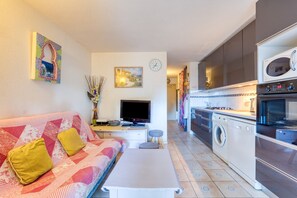 Un espace de vie compact comprenant un canapé, un téléviseur, un lave-linge et une kitchenette.