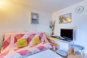 Une chambre à coucher avec un lit, un bureau avec un ordinateur, une télévision et une horloge au mur.