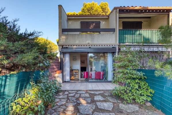 Une maison à deux étages avec un chemin de pierre menant à l’entrée, un balcon et un jardin clos.