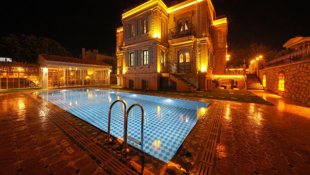 Ein Gebäude bei Nacht mit Schwimmbecken, Steinmauern und beleuchteten Balkonen.