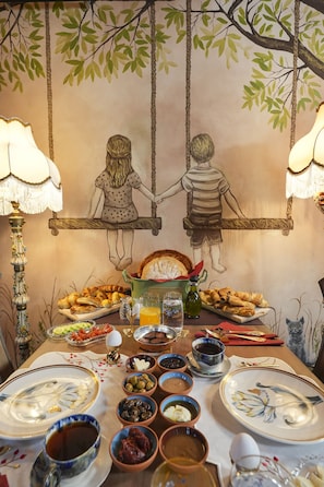 A dining table set with various dishes and a mural of children on a swing. - Naz Su Cunda (Ayvalik)