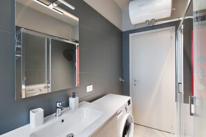 Ein modernes Badezimmer mit großem Spiegel, Waschbecken, Waschmaschine und Duschkabine.