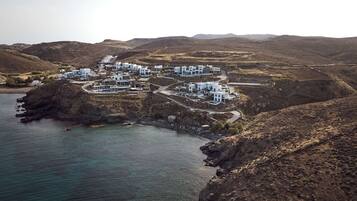 A coastal village with white buildings arranged in a circular pattern around a central area, connected by winding roads.
