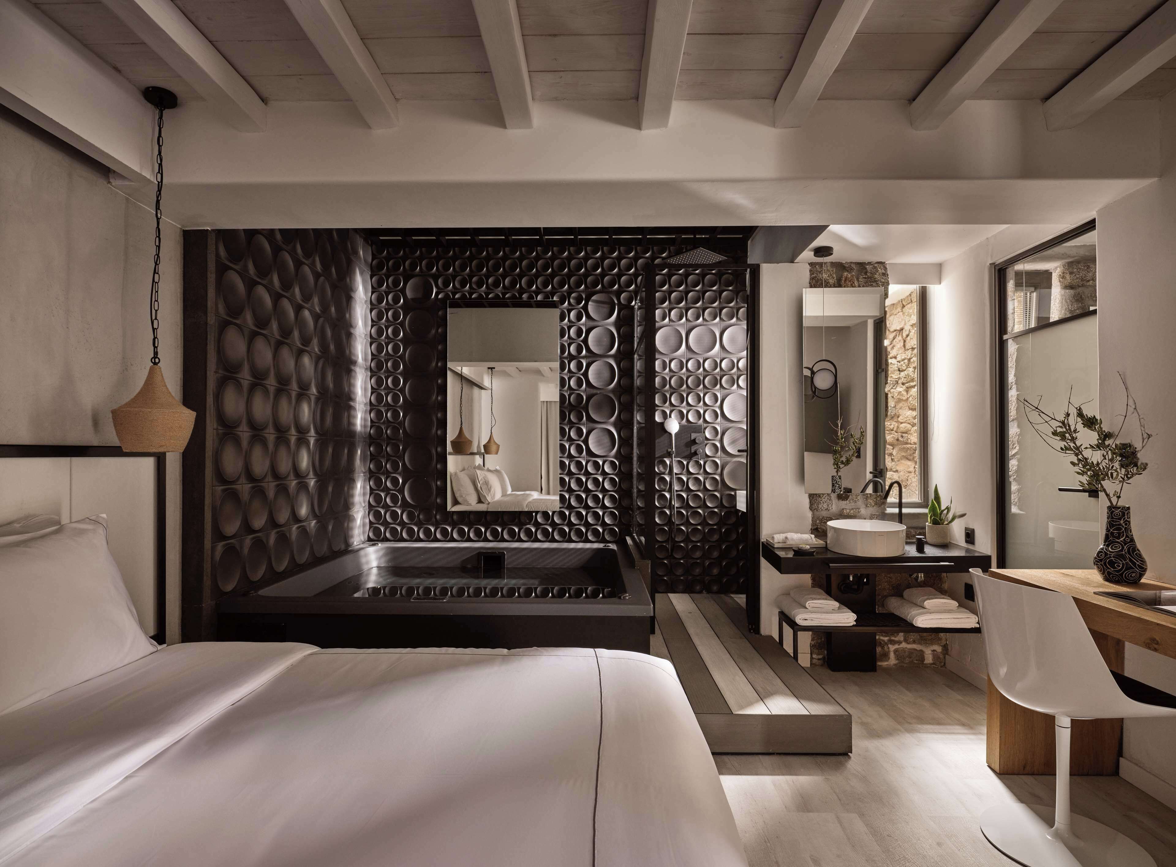 A modern bedroom with a large bed, a built-in bathtub, a vanity with a mirror, and a desk with a chair.
