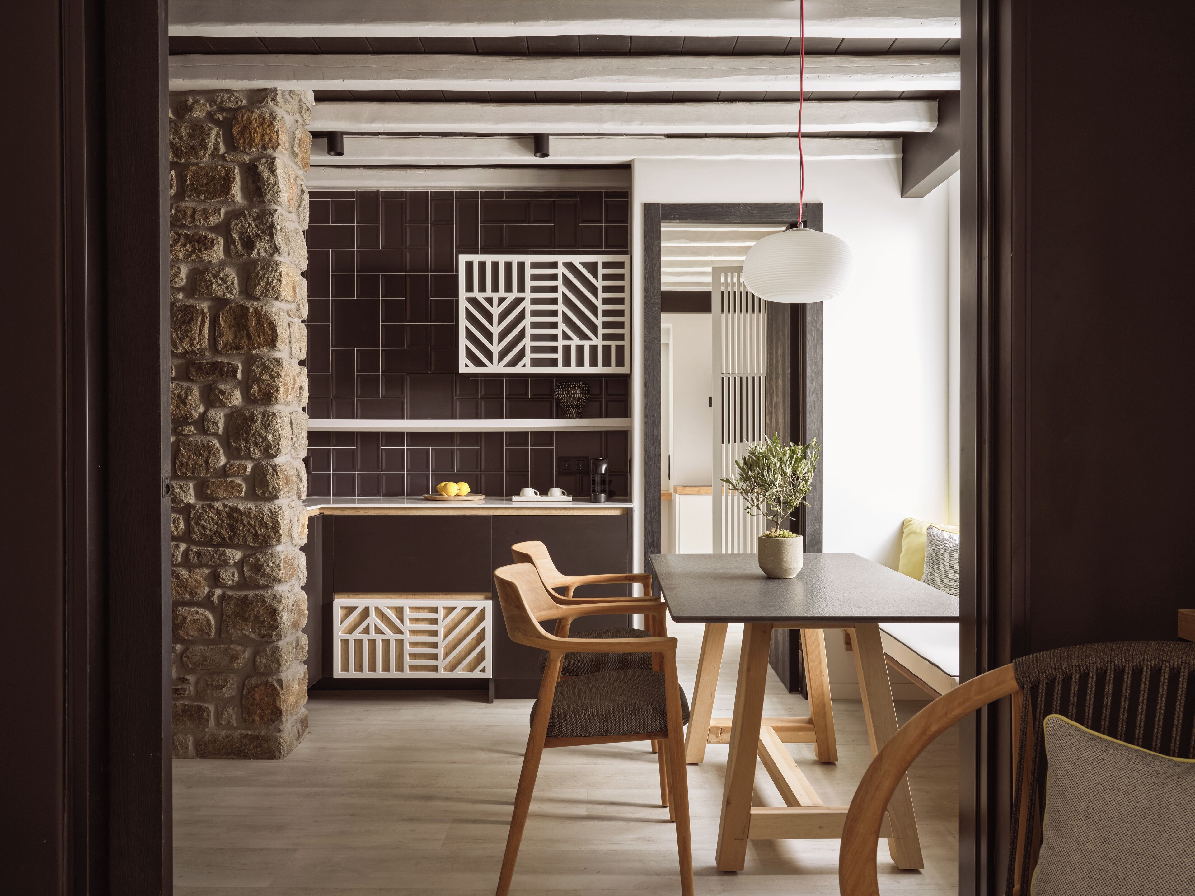 A modern kitchen with a stone wall, dark tiles, and a wooden dining table with chairs.