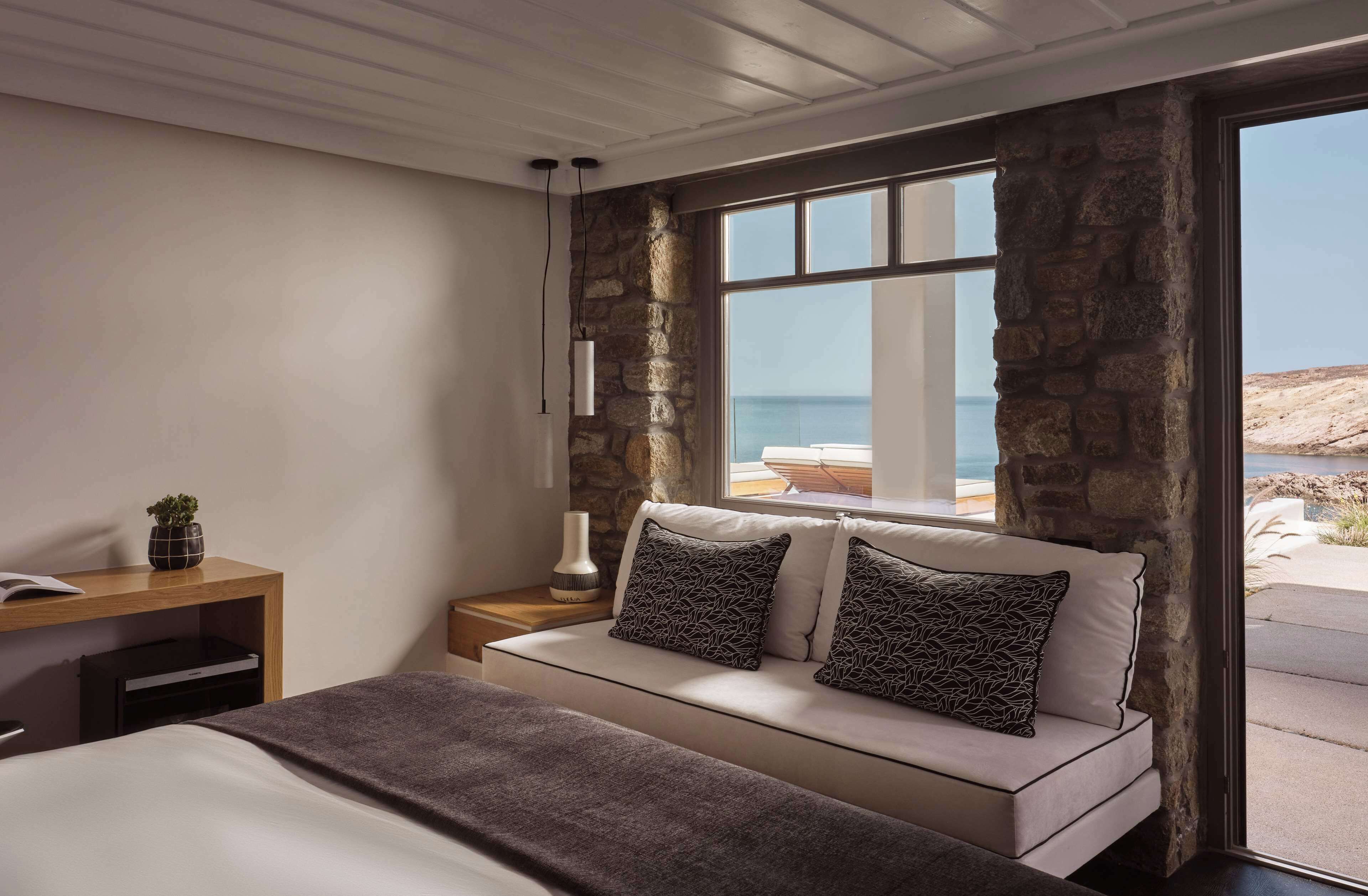 Een slaapkamer met een bed, nachtkastje, lamp en uitzicht op zee.