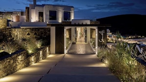 A modern building with a stone facade, a central entrance, and a pathway leading to the entrance. - Semeli Coast Mykonos, Curio Collection by Hilton (Mykonos)