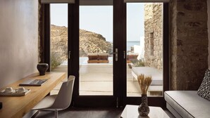 A modern interior with a large sliding glass door leading to a balcony overlooking a mountainous landscape and the sea. - Semeli Coast Mykonos, Curio Collection by Hilton (Mykonos)