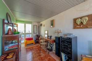 Een kamer met een naaimachine, een houten kast met servies, een tafel met een gele tafelkleed en een spiegel aan de muur.
