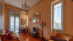 Uma sala de estar com sofá, televisão, lustre e um espaço de jantar com cadeiras e mesa.