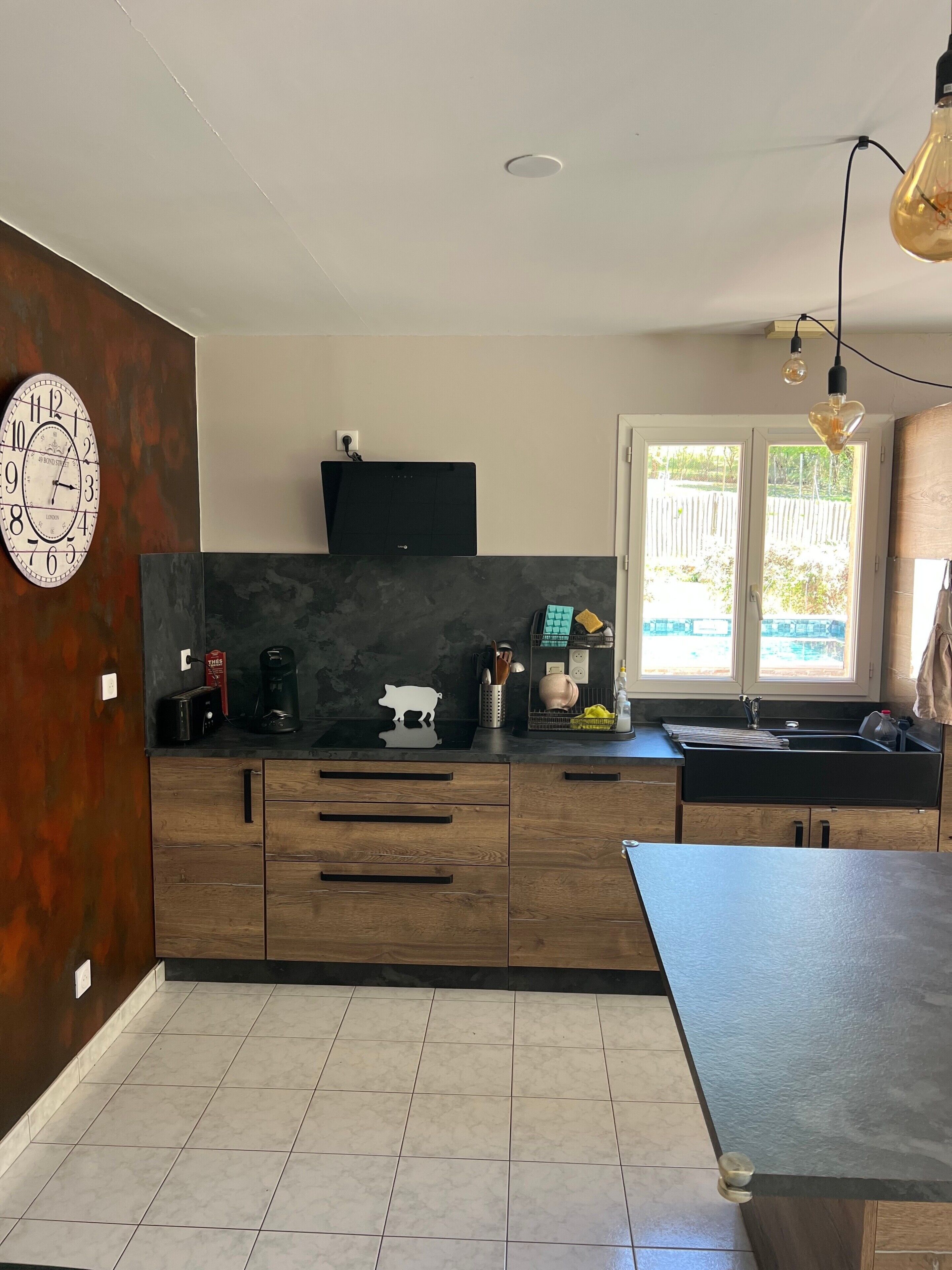 A modern kitchen with wooden cabinets, a black countertop, a built-in oven, and a window with a view of the outdoors.