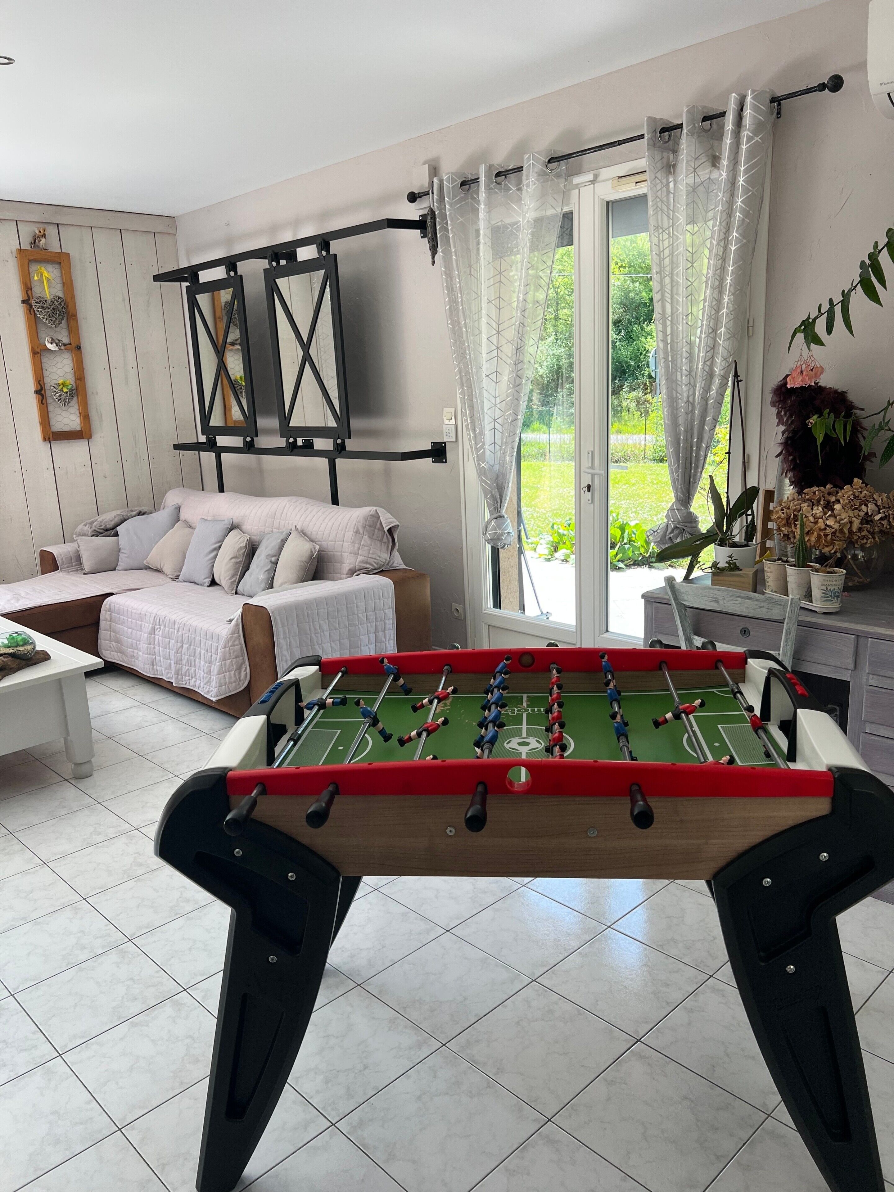 A living room with a foosball table, a sofa, a coffee table, and a window with curtains.